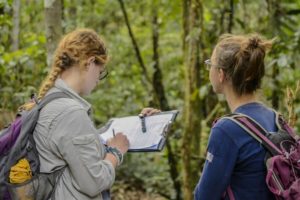 Two environmental volunteers observing wildlife in the Peruvian rainforest and taking notes.